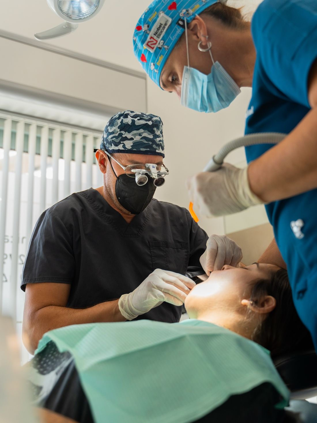 Dentista con lupas de aumento realizando un tratamiento junto a su asistente